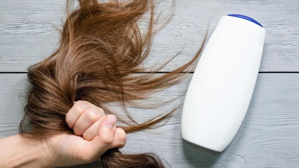 Hair strands in a woman hand with bottle of shampoo