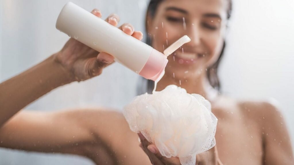 A woman pouring body wash on a shower loofah