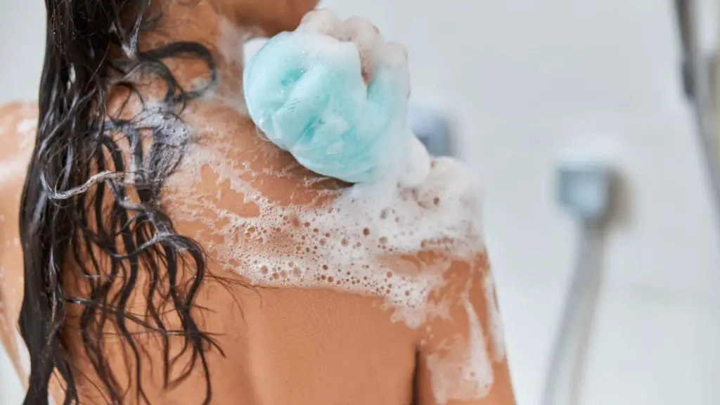 Woman applying body wash with a blue shower loofah